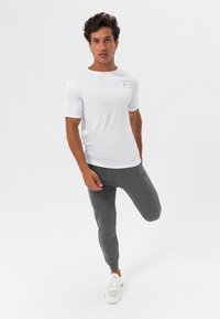 Fehér, rövid ujjú sportpóló, szürke, slim-fit joggingnadrággal párosítva, rugalmas derékpánttal és fehér sportcipővel. Sima szövettextúra.