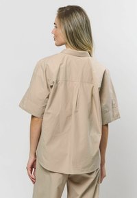 Világos bézs színű, rövid ujj�ú ing, álló gallérral, hátul yoke varrással és puha, texturált anyaggal.