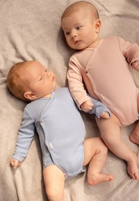 Två spädbarn i ribbade sparkdräkter; en i ljusblått och den andra i mjukt rosa. Båda har långärmat och tryckknappar och ligger på en grå filt.