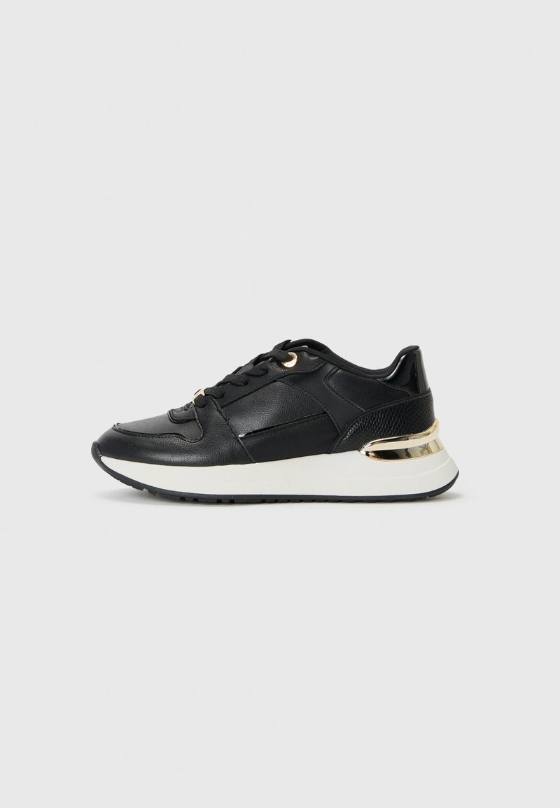 Zwarte sneaker met een gestructureerde leren bovenkant, gouden accenten op de hiel, vetersluiting en een witte tussenzool voor contrast.