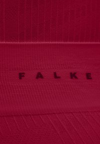 Czerwona dziana tkanina z ryżowym i teksturowanym wzorem, z nazwą marki "FALKE" wytłoczoną w ciemnoczerwonym kolorze.