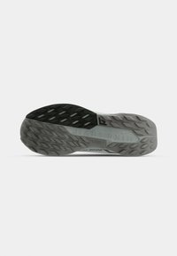 Semelle de chaussure de trail avec une surface en caoutchouc gris texturé et des crampons multidirectionnels pour une meilleure traction. Marque visible sur le côté.