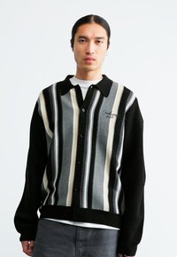 Cardigan a righe nere e grigie con chiusura a bottoni, maniche a contrasto, texture morbida e logo ricamato sul petto.