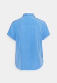 Koszula z krótkim rękawem w jasnoniebieskim kolorze. Posiada kołnierz, zaokrąglony dół oraz subtelną poświatę. Gładka faktura bez widocznych wzorów czy akcentów.