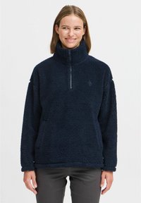 Marineblå fleece-pullover med høy krage, halv-glidelås og teksturert overflate. Har en avslappet passform og synlige sømdetaljer.