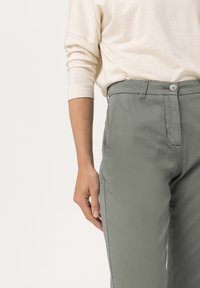 Lehké zelené bavlněné kalhoty se s rovný střih, které mají přední zapínání na knoflík a boční kapsy. Hladká textura, minimální detaily šití.