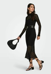 Černé krajkové šaty s přiléhavým střihem, dlouhými rukávy a průsvitným spodkem. Doplněné černým páskem a černou texturovanou kabelkou.