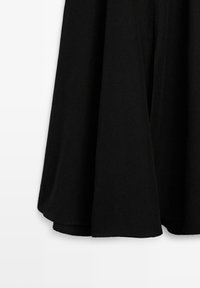 Jupe en coton noire au design évasé, avec une texture lisse et une forme en A. L'ourlet est arrondi et se situe au-dessus du genou.