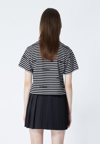 Randig svart och vit kortärmad t-shirt, kombinerad med en plisserad svart kjol. Tydlig text på t-shirten nära fållen.