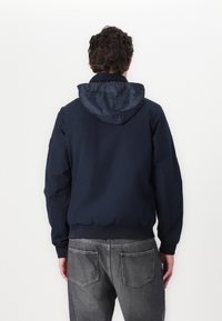 Giacca blu navy con cappuccio, realizzata in materiale liscio. Polsini e vita elasticizzati, presenta un design semplice e lineare.