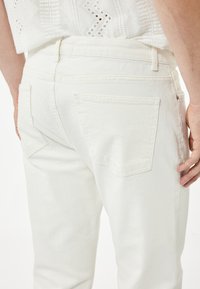 Valkoiset farkut, joissa on takataskut, suora malli, näkyvät saumat ja sileä pinta. Vyötärö on korkea ja siinä on vyölenkit.