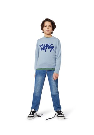 Pull bleu clair avec un grand texte graphique bleu marine, superposé sur une chemise verte. Associé à un jean bleu et des baskets noires avec des semelles blanches.