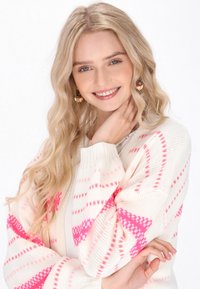 Bela pletena cardigan s roza vzorcem, ribanim zaključkom in sproščenim krojem. Nosita jo čez lahkotno majico, v kombinaciji s krožnimi uhani.