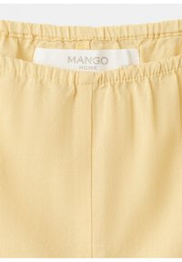 Tissu à ceinture élastique jaune pâle avec des coutures visibles et une étiquette blanche de la marque Mango Home cousue à l'intérieur.