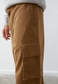 Pantalones de algodón marrón con un bolsillo lateral tipo cargo y una textura suave, con piernas rectas y un ajuste moderno.