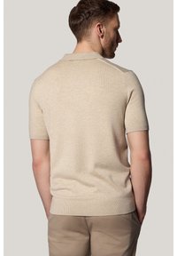 Beżowa, krótką rękawów, dziana koszulka polo z subtelną fakturą i prążkowanym kołnierzykiem, charakteryzująca się dopasowanym fasonem i prostymi liniami.