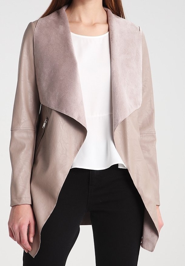 Chaqueta de imitación de cuero taupe claro con cuello de ante, apertura frontal y dos bolsillos laterales con cremallera. Llevada sobre una blusa blanca y pantalones negros.