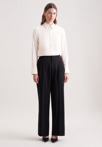 Light cream blouse with a pointed collar and long sleeves paired with high-waisted, wide-leg black trousers and pointed black heels.