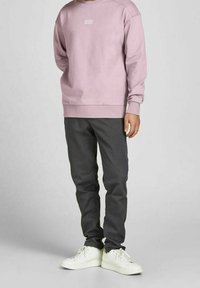 Ljusrosa sweat-shirt med en vit logotyp, matchad med mörkgrå byxor och vita sneakers. Tyget ser mjukt ut med ribbade ärmslut.