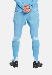 Completo sportivo azzurro chiaro con maniche lunghe, pantaloni corti abbinati e calze blu con strisce bianche. Scarponi neri con accenti dorati.