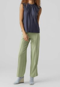 Camicetta senza maniche blu marina con colletto arricciato, abbinata a pantaloni a gamba larga verde chiaro. La modella indossa calzini con righe blu e scarpe con zeppa.