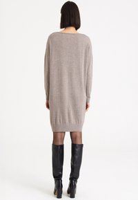 Överdimensionerad beigefärgad stickad klänning med vid halsringning, långa ärmar och ribbad nederkant. Matchad med knähöga svarta läderstövlar.