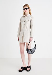 Beige skjortekjole med knapper og to brystlommer, satt sammen med svarte platåsandaler og en strukturert svart håndveske.