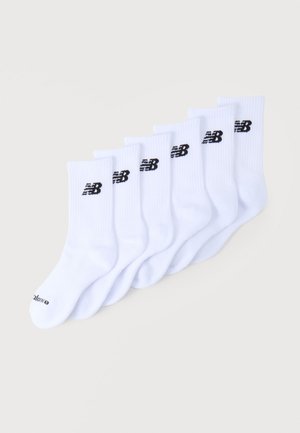 Kuuest valgest meessukapaari, millel on mustad New Balance’i logod, diagonaalselt kuhjatud heledal taustal.