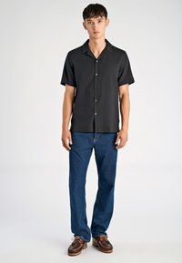 Maglietta nera a maniche corte con chiusura a bottoni, abbinata a jeans blu dritti e scarpe da barca marroni. Tessuto strutturato, vestibilità rilassata.