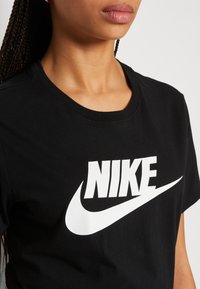 Zwarte katoenen T-shirt met een groot wit Nike-logo op de voorkant. Het shirt heeft een klassieke ronde hals en een relaxte pasvorm.