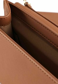 Bruine leren tasinterieur met een gladde textuur, met een ritsvak en een gevoerd gedeelte. Gestikte details zijn zichtbaar.