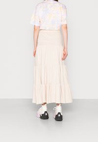 Beige gelaagde maxi rok, gecombineerd met een pastel tie-dye t-shirt. Schoeisel heeft zwarte, witte en roze accenten met sterdetails.