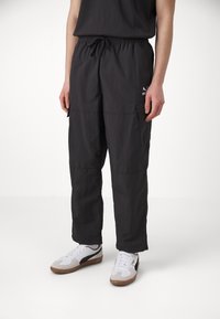 Zwarte cargo-broek met een elastische tailleband, lichtgewicht materiaal, twee zijzakken en een klein logo bij de heup. Geschikt voor casual kleding.