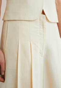 Crème kleurige tailleurbroek met plooien, gemaakt van textiel met een structuur. Het ontwerp heeft een hoge taille en minimaal zichtbare naden voor een strakke uitstraling.