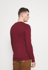 Burgunderfarbener Rundhals-Pullover aus weichem Strickmaterial, mit langen Ärmeln und einer figurbetonten Silhouette, mit gerippten Bündchen und Saum.