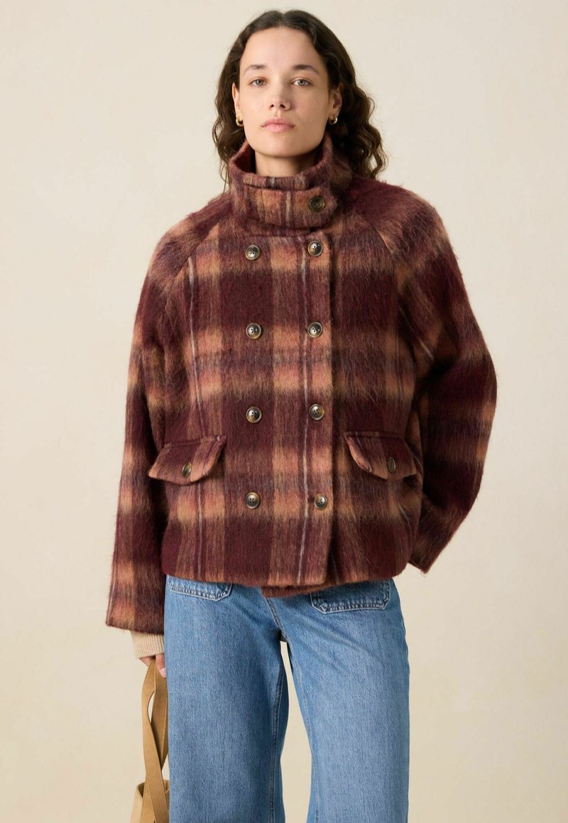 Veste à carreaux bordeaux et beige en tissu texturé, avec un col montant, des boutons double boutonnage et deux poches avant.