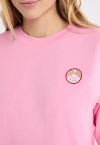 Roze sweatshirt met een ronde geborduurde patch met bergen, sterren en de tekst "SKI." Zacht materiaal met een klassieke ronde hals.