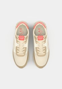 Beige and cream sneakers with light mesh and leather accents, featuring beige laces and a coral logo on the tongue. Textured sole.