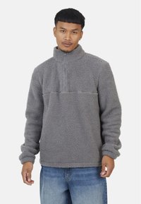 Szary polarowy sweter z pół-zamkiem, o teksturowanej tkaninie, długimi rękawami i poziomą szwem wzdłuż klatki piersiowej. Casualowy design.
