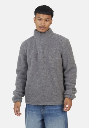 Gray fleece pullover with a half-zip collar, textured fabric, long sleeves, and a horizontal seam across the chest. Casual design.