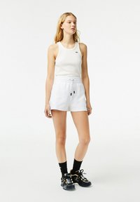 Canottiera bianca atletica e pantaloni corti con una cintura elastica. Sneakers nere e oro con dettagli intricati e calzini neri.