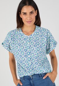 Blusa de manga corta, abotonada, en tejido azul claro con un patrón floral en tonos verdes y azules y un cuello redondo.