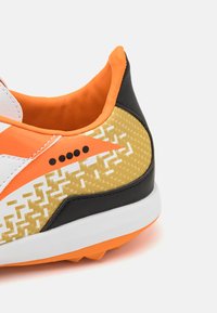Zapatilla deportiva con cordones en un diseño negro, blanco y naranja; cuenta con un patrón geométrico texturizado en oro y blanco en el talón.