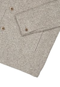 Beżowa kurtka w wzór houndstooth wykonana z teksturowanej tkaniny, z dwoma guzikami, kołnierzykiem i kieszenią z przodu.