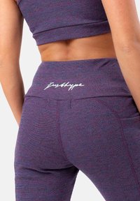Leggings viola a coste con vita alta che presentano il testo bianco "Just Hype". Include tasche laterali, tessuto testurizzato con una leggera lucentezza.