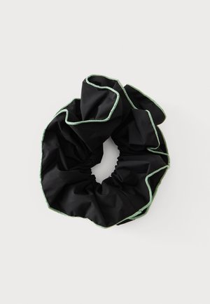 Chouchou en tissu noir avec bords cousus vert clair sur un fond uni clair.