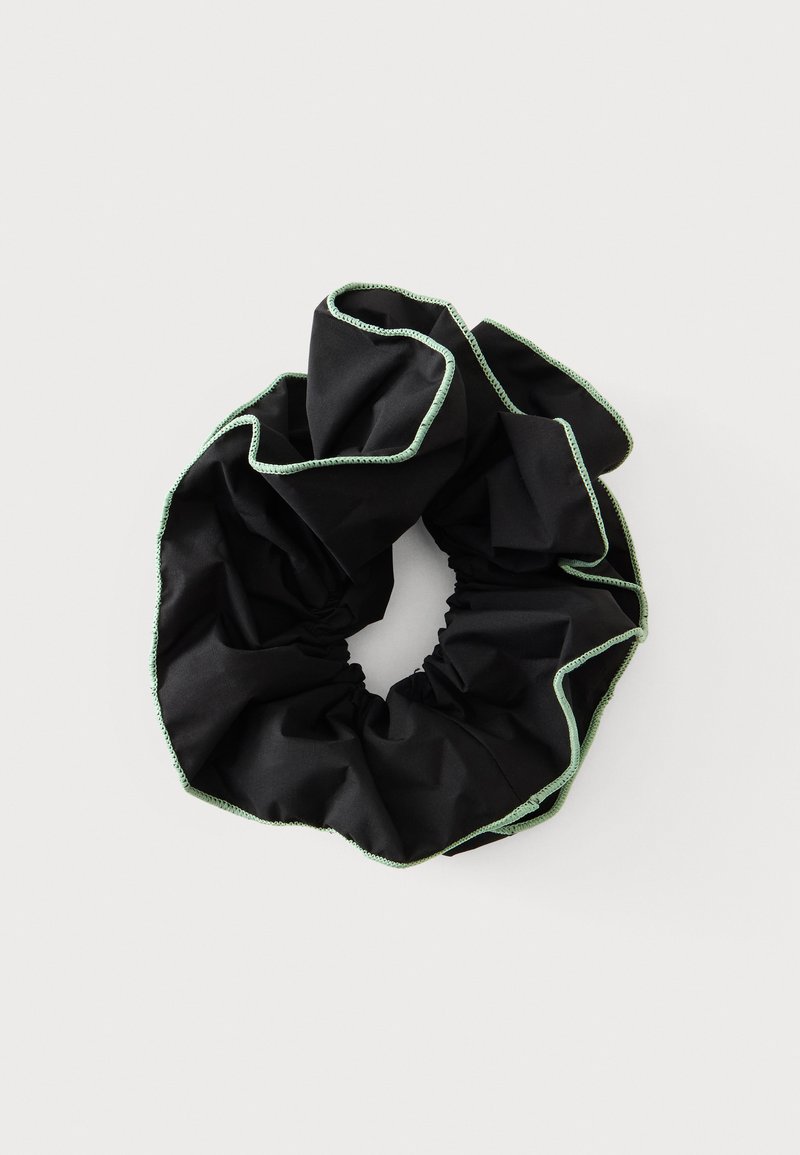 Chouchou en tissu noir avec bords cousus vert clair sur un fond uni clair.