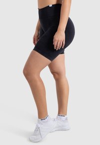 Zwarte high-waisted shorts van zacht materiaal, met een aansluitend ontwerp en een gladde textuur, gecombineerd met witte sportschoenen en sokken.