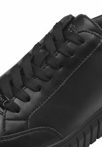 Black leather shoe with textured surface, featuring round laces, padded collar, and a treaded rubber sole. Accent logo near the eyelet.