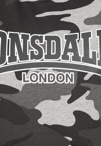 Pelēka un melna kamuflāžas raksta audums ar izteiksmīgu "LONSDALE" tekstu virs "LONDON" baltā krāsā. Uzsver sportisku estētiku.